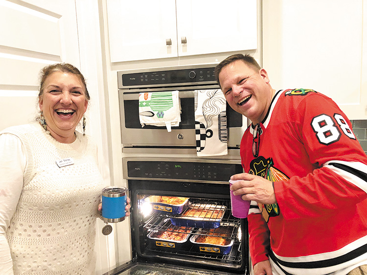 Hosts Jan Storey and Jon Swanson, ready to bring more pans of homemade lasagna to the buffet; photo by Camille Esterman