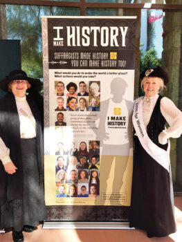 Questers Anne Levig and Debbie Hansen are dressed as suffragists beside the Questers Women’s Suffrage Centennial Exhibit.