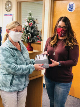 Betty Ryan safely distributing gift certificates for children and families to Lydia Smith of Mountain Vista school in Oracle.